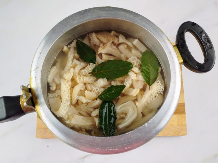 Bucho em uma panela de pressão coberto por água e com folhas de louro.