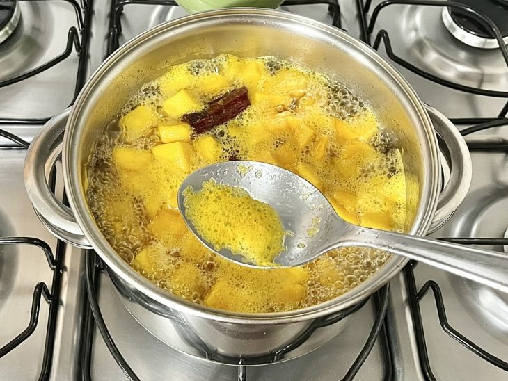 Uma panela contendo calda de açúcar cozinhando mangas picadas.