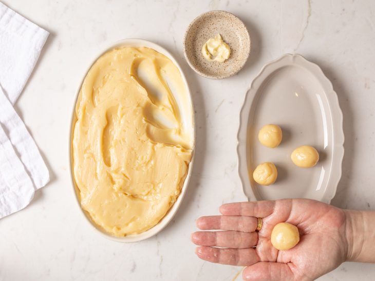 Partes do doce sendo retiradas para fazer bolinhas com a mão untada de manteiga.