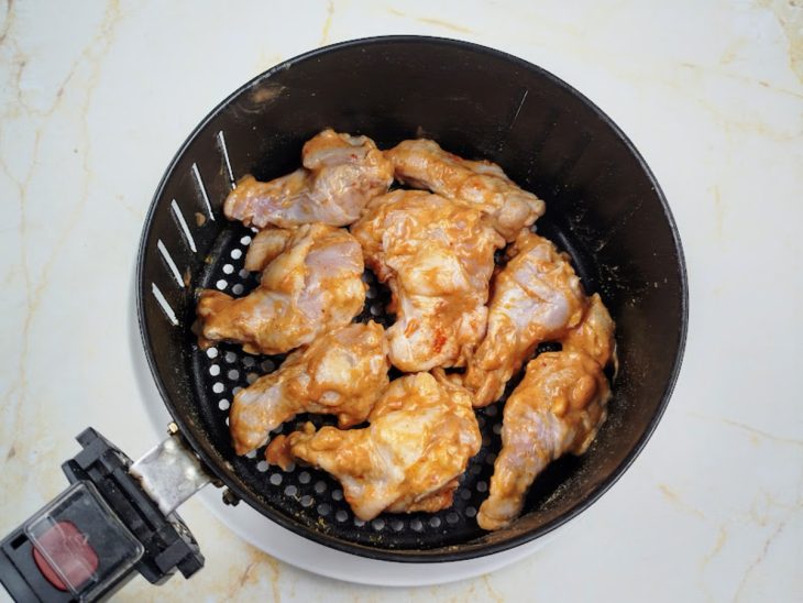 Uma cesta de air fryer com o frango cru.