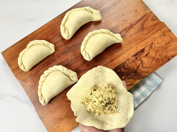 Uma tábua com empanadas sendo recheadas e montadas.