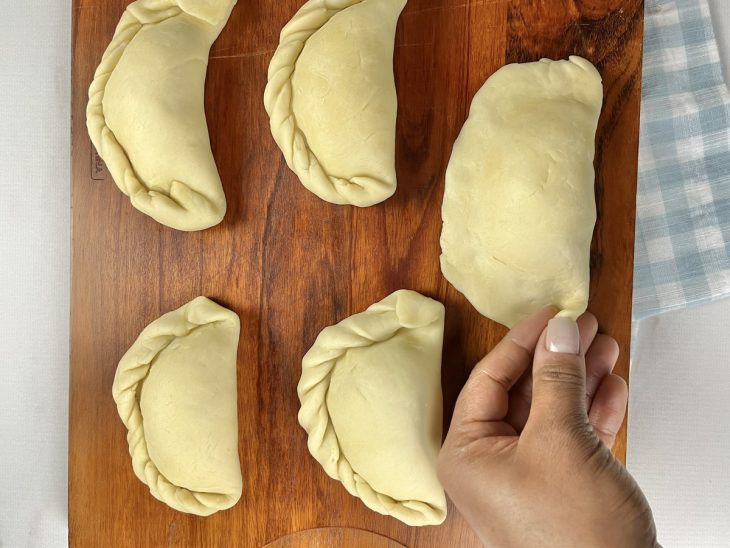 Uma tábua com empanadas sendo recheadas e montadas.