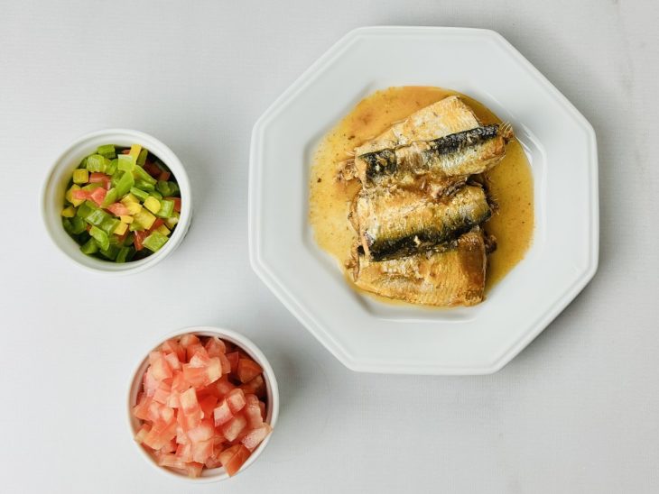 Um prato com sardinha e recipientes com pimentão e tomate picados.