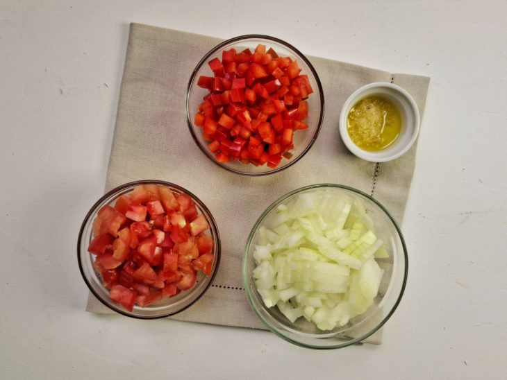 Alho, cebola, pimentão e tomate cortados em recipientes.