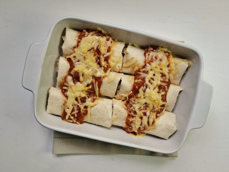 Enchiladas em uma travessa com molho e queijo adicionados por cima.