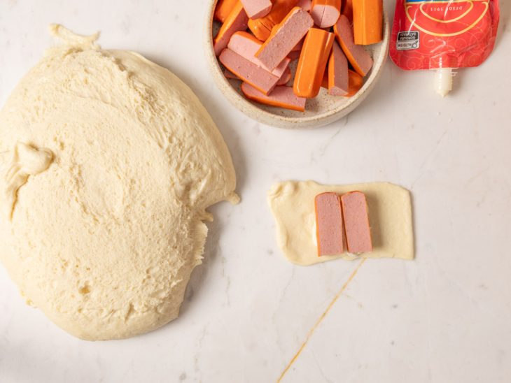 Um pedaço da massa sendo recheado com salsicha e Catupiry.