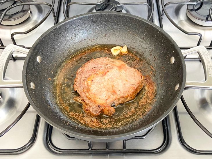 Alho, manteiga e fatia de carne dourando em uma frigideira.