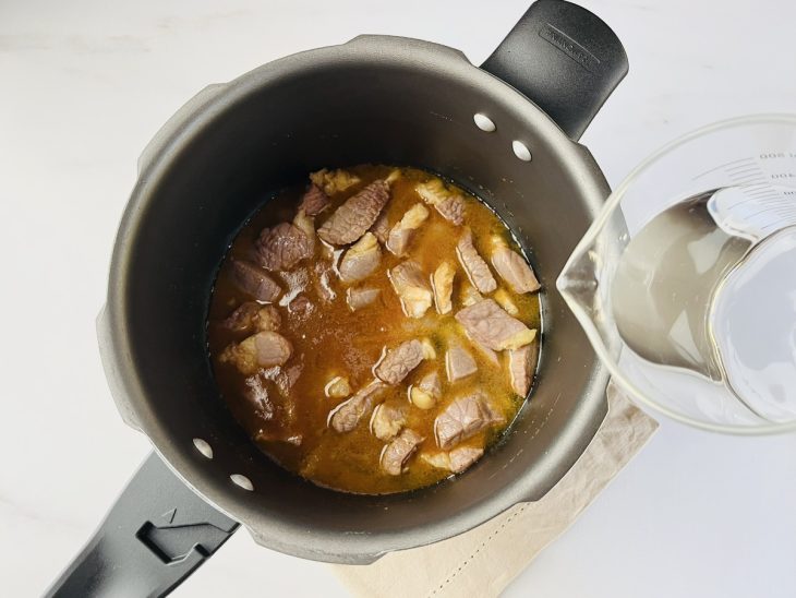 Uma panela de pressão com banha, cebola, alho, charque e temperos.