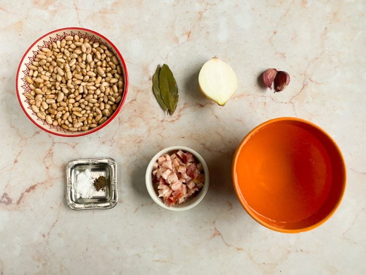 Todos os ingredientes necessários para o preparo do feijão-carioca dispostos em uma mesa.