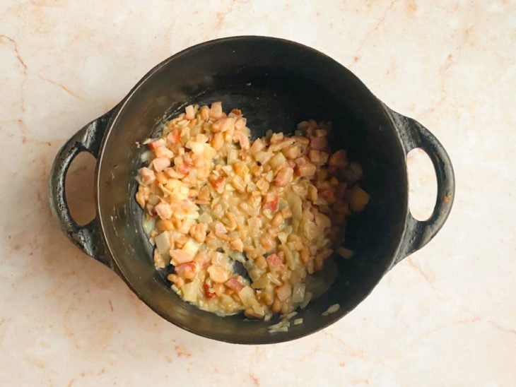 Panela com cubos de bacon, cebola, alho e o feijão que estava reservado.