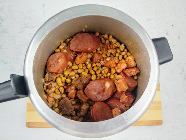 Uma panela de pressão com as carnes, feijão e temperos.