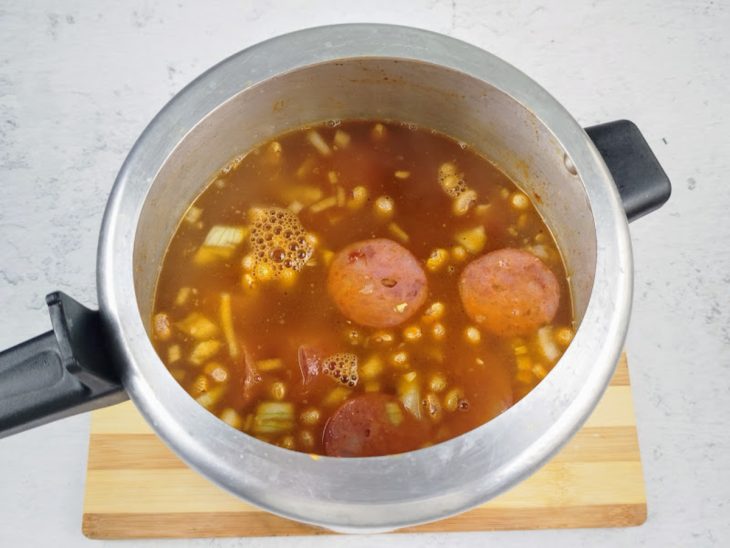 Uma panela de pressão com as carnes, feijão, água e temperos.