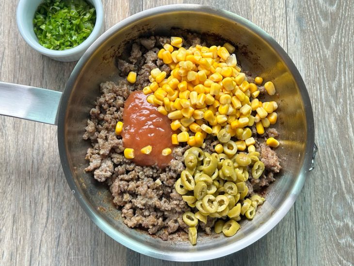 Panela com carne, milho, azeitona, cebolinha e molho de tomate.