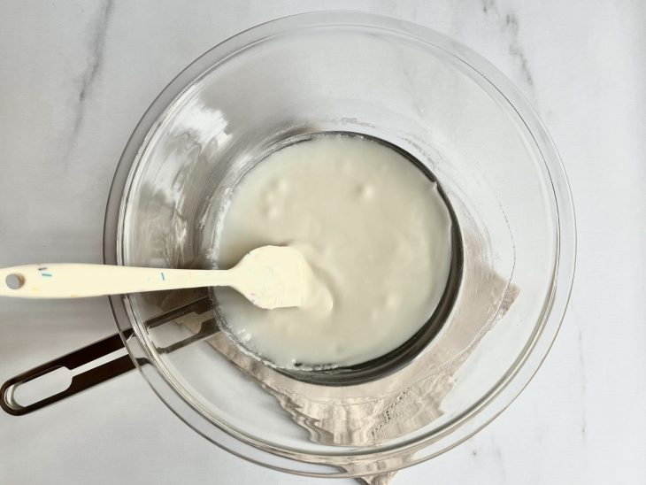 Uma tigela com a mistura de açúcar e leite sobre uma panela com água quente.