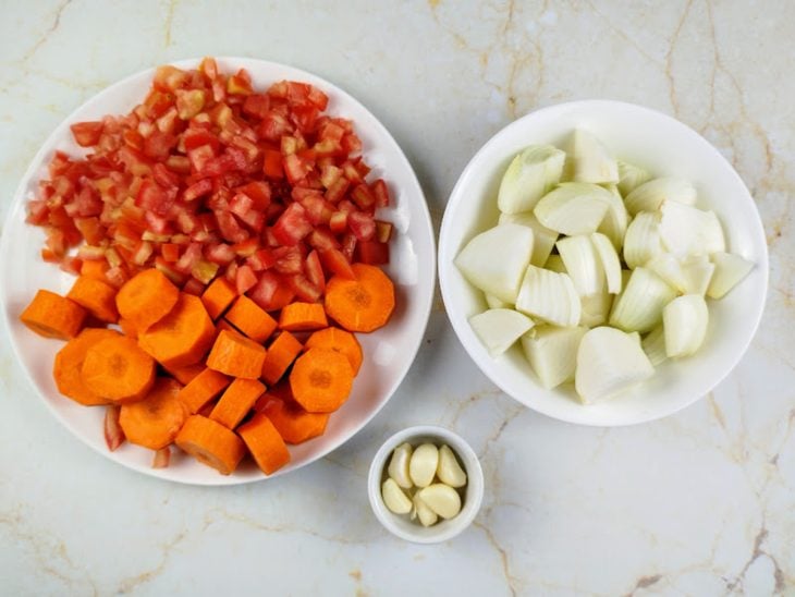 Recipientes contendo cenoura, tomate, cebola e alho picados.