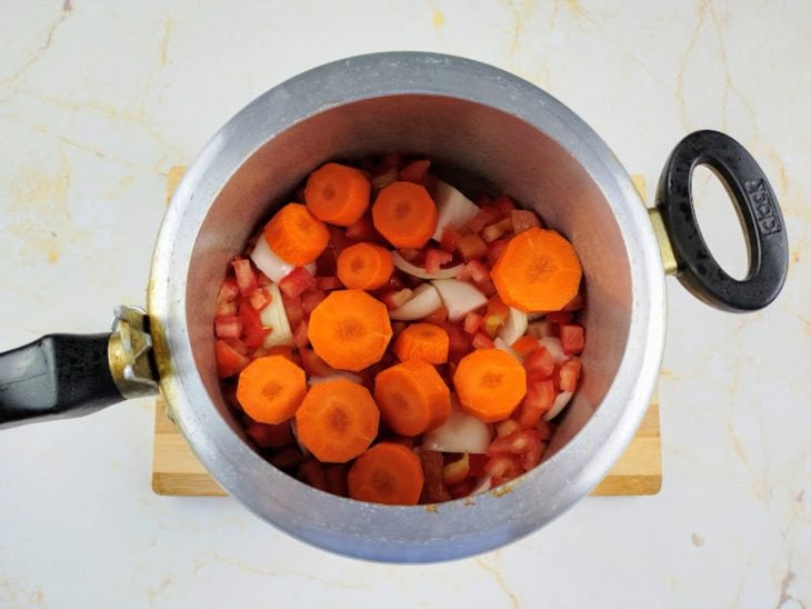 Uma panela de pressão com cebola, alho, cenoura e tomate.