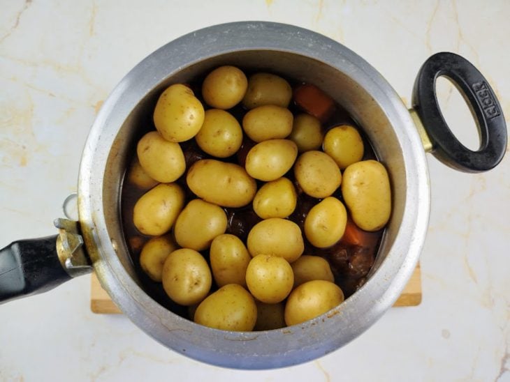 Uma panela de pressão com todos os ingredientes e a adição das batatas bolinhas.