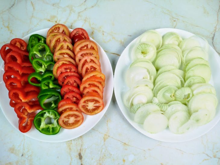 Pratos com pimentão, cebola e tomate fatiados.