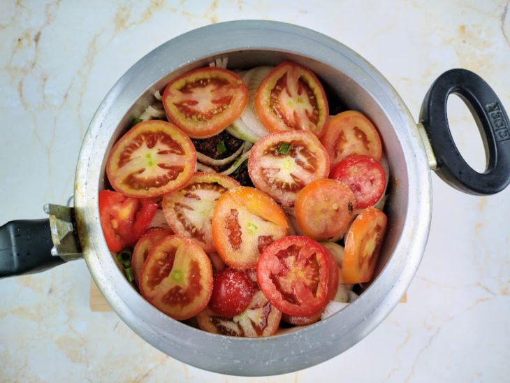 Uma panela de pressão com uma camada de cebola, pimentões, tomate, fraldinha e temperos.