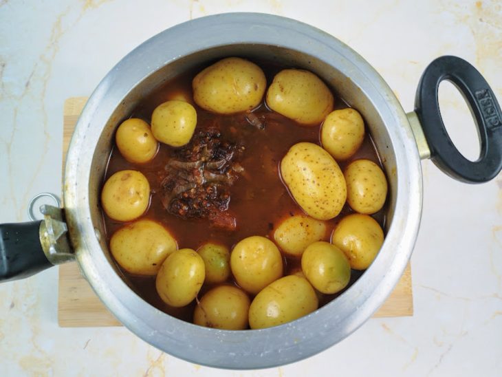 Uma panela de pressão com a fraldinha cozinhando com as batatinhas.