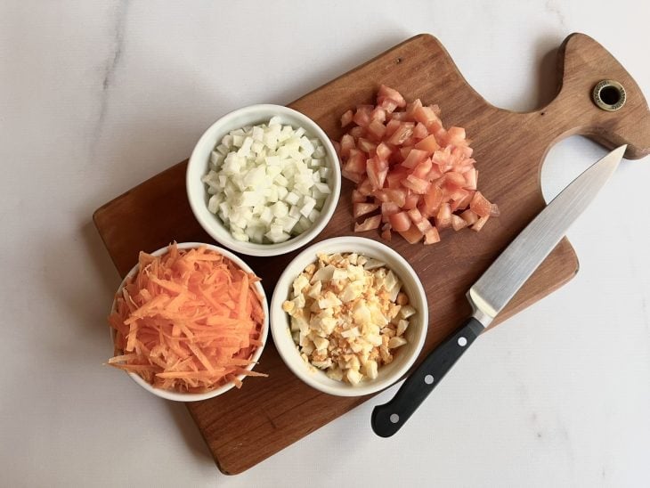 Ovo, tomate e cebola picados e cenoura ralada em uma tábua.