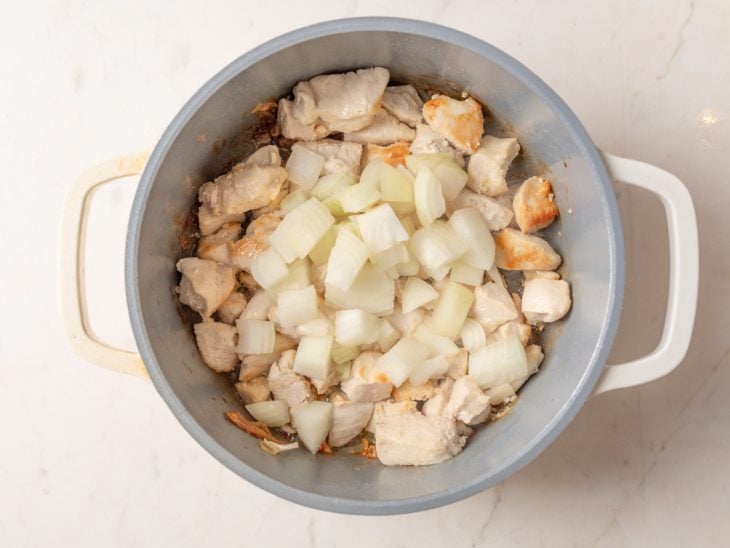 Uma panela com o frango e a cebola picada refogando.