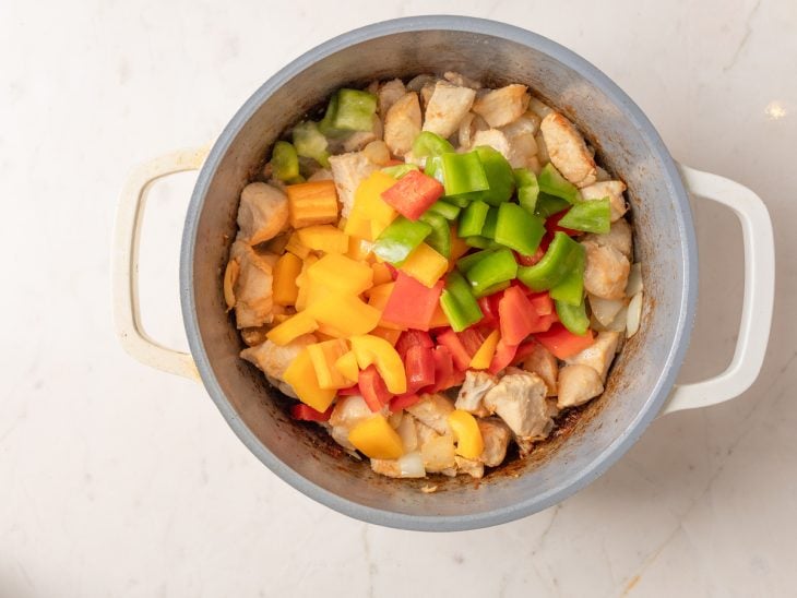 Uma panela com frango, cebola e pimentões cozinhando.