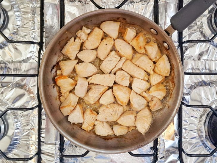 Cubos de frango refogados no azeite em uma frigideira.