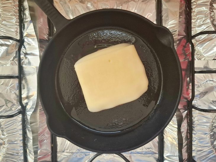 Uma frigideira fritando um hambúrguer de carne com queijo em cima.