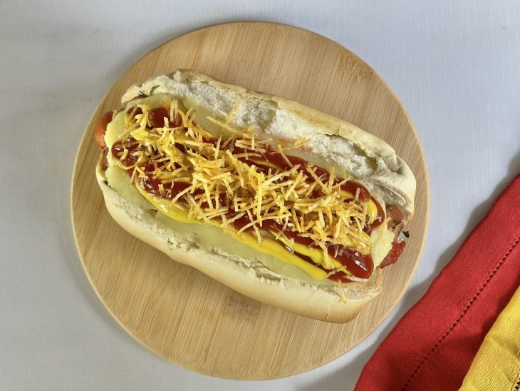 Um pão com salsicha, molho, vinagrete, purê, mostarda, ketchup, batata palha.