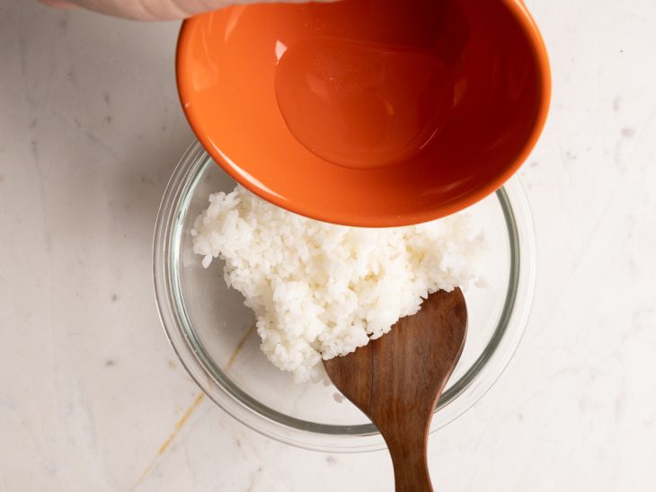 Arroz de sushi cozido e reservado em uma tigela com o tempero sendo adicionado.