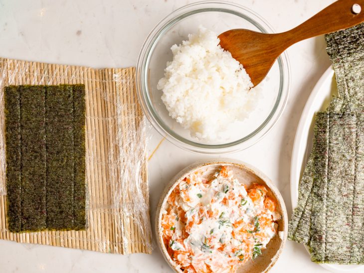 Esteira de sushi com alga sobreposta, arroz e patê de salmão ao lado.