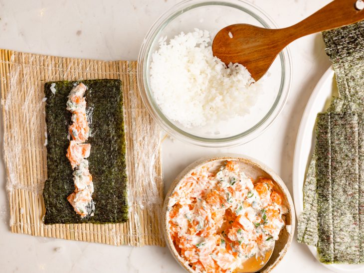 Alga com camada de recheio de salmão acomodada ao meio, com o arroz virado para baixo.