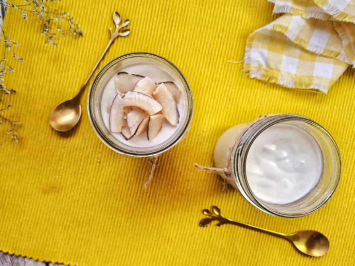 Pote de iogurte grego natural vegano com pedaços de coco em cima.