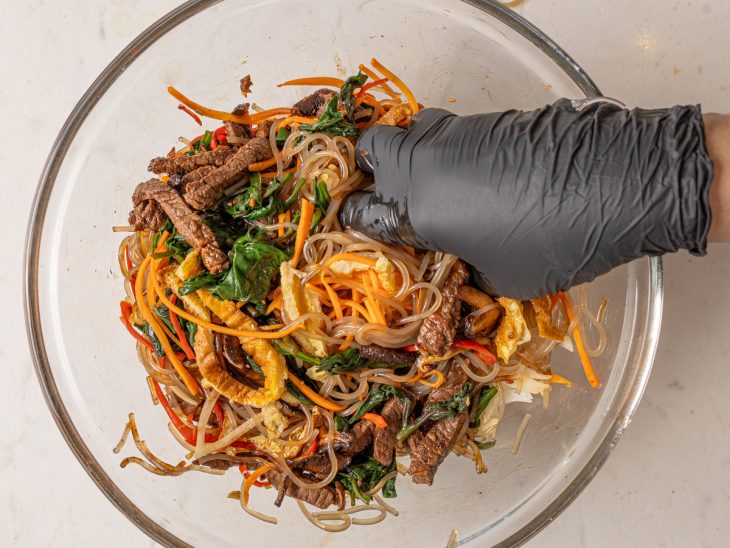 Uma tigela com os ingredientes do japchae sendo misturados.