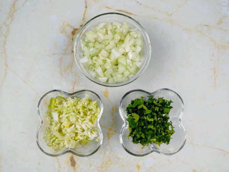 Recipientes com cebola, alho-poró e cheiro-verde picados.