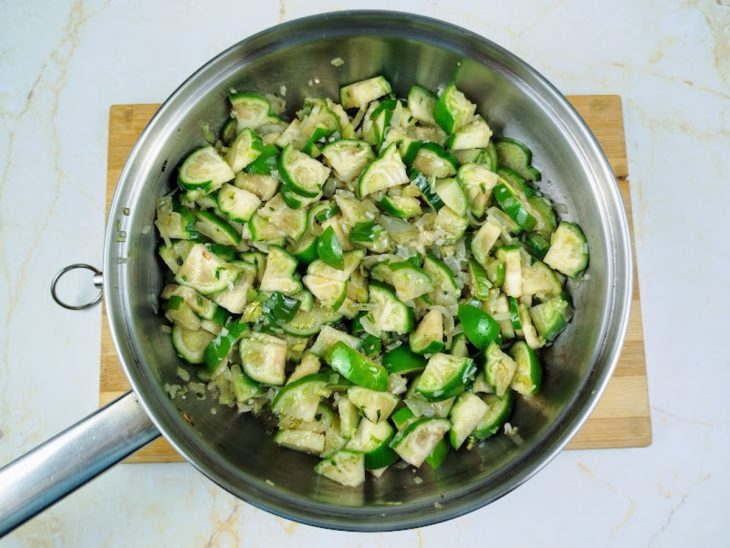 Uma frigideira com jiló, azeite, cebola, alho, cheiro-verde, sal e pimenta.