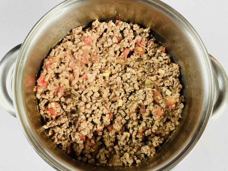 Uma panela com carne, azeite, cebola, alho, tomate, pimentão e temperos.