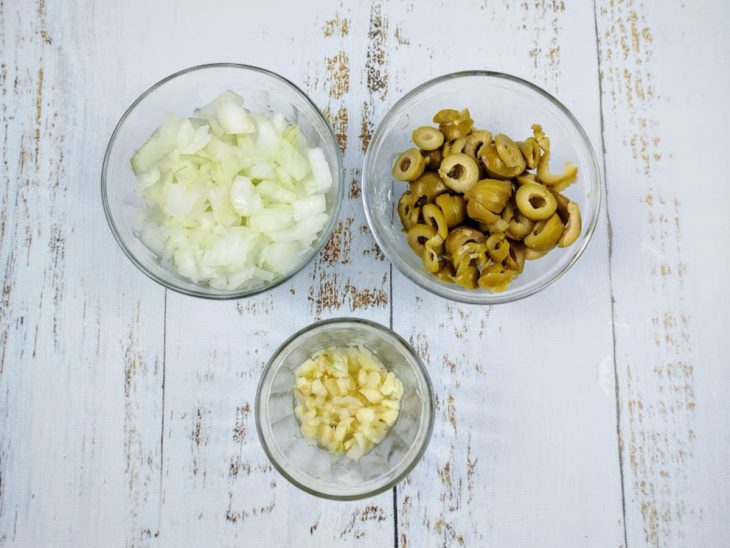 Recipientes com cebola, azeitonas e alho picados.