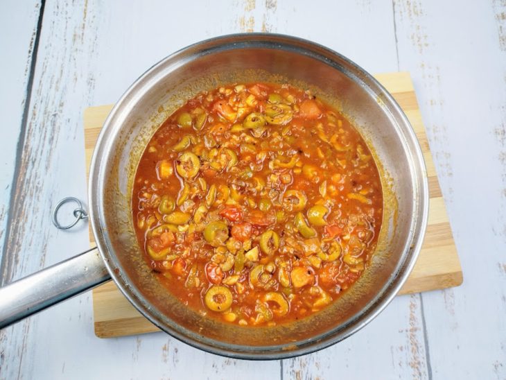 Uma panela com molho de tomate, azeitonas, alho, cebola e temperos.