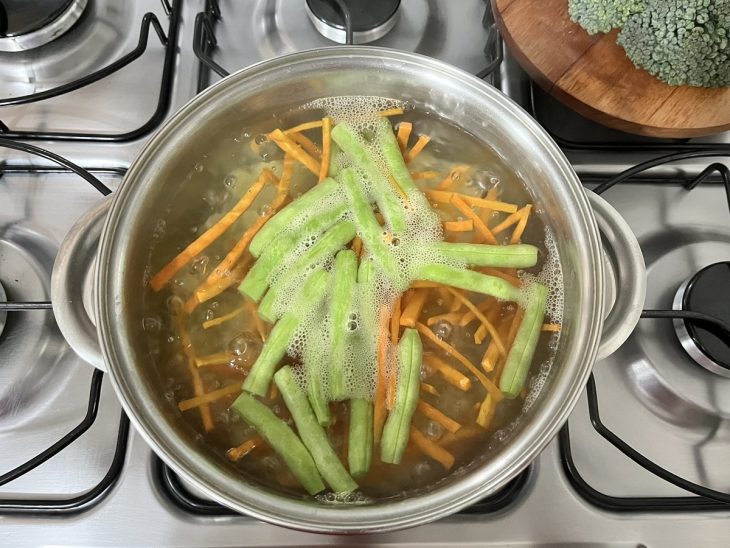 Panela com cenoura e vagem cobertos por água.