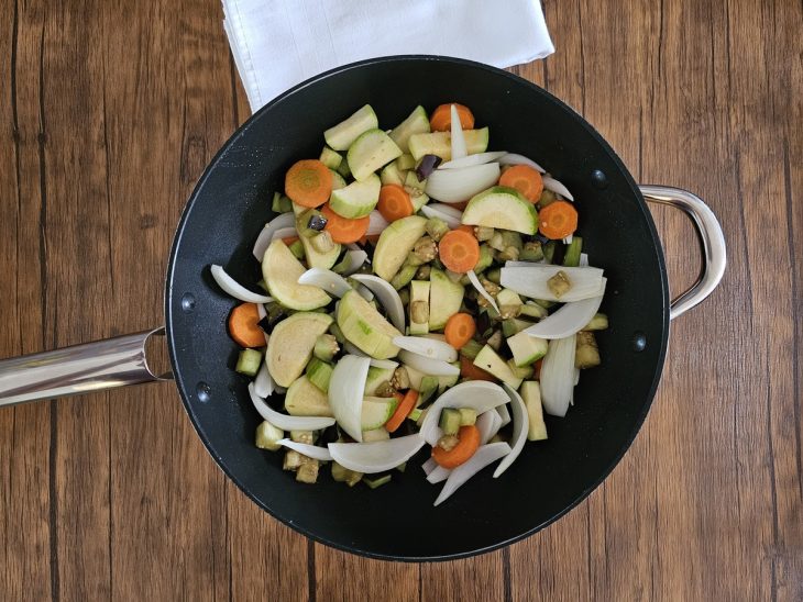 Uma frigideira com azeite, cenoura, berinjela, abobrinha e cebola.