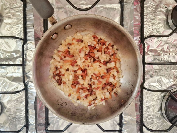 Uma panela com banha, bacon e cebola a dourar.