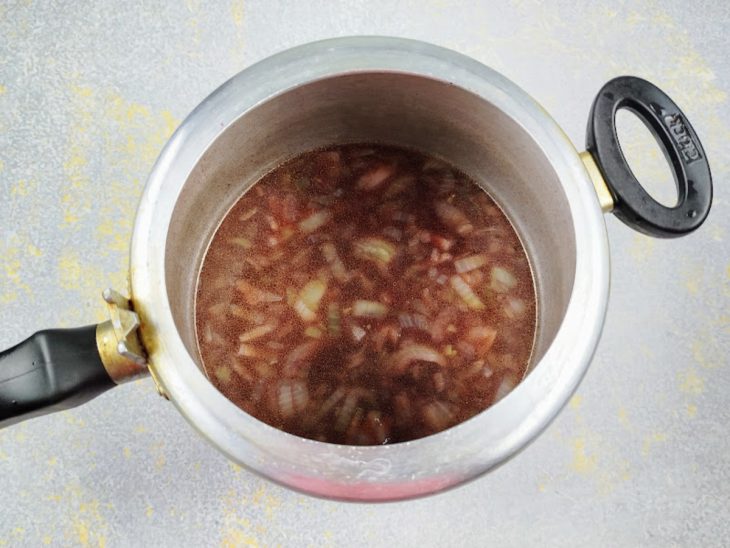 Uma panela de pressão com azeite, cebola, alho, molho de tomate, vinho e caldo de carne.