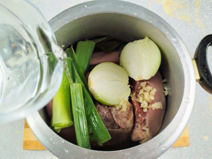 Uma panela de pressão com línguas de boi, cebola, alho e folhas de alho-poró.