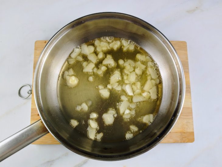 Azeite aquecido e lâminas de alho na frigideira.