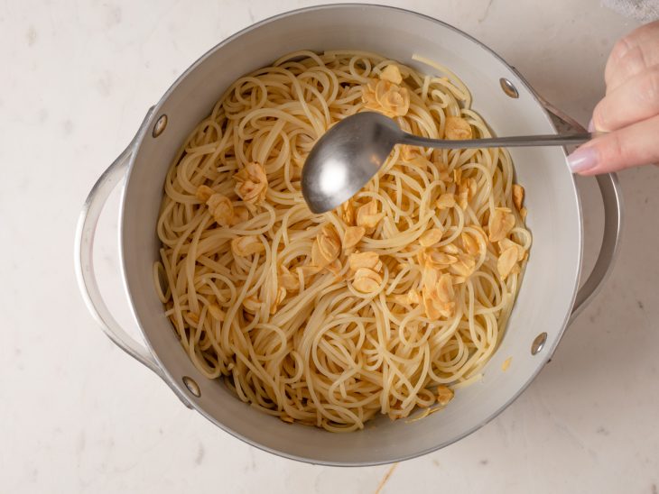 Macarrão acomodado na panela com lâminas de alho e conchas de água adicionadas.