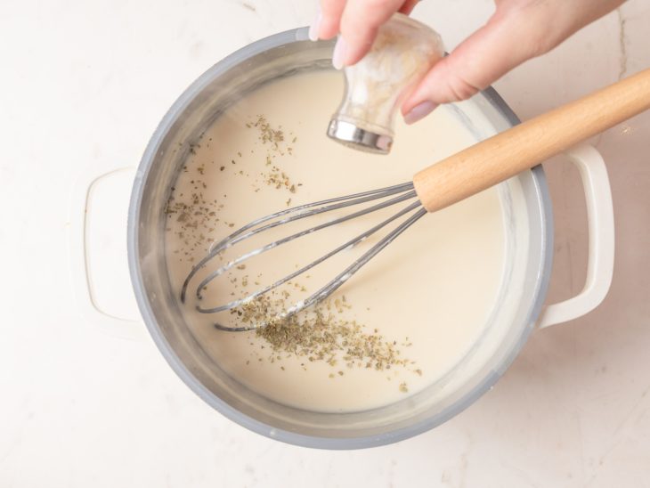 Molho branco sendo temperado com orégano.