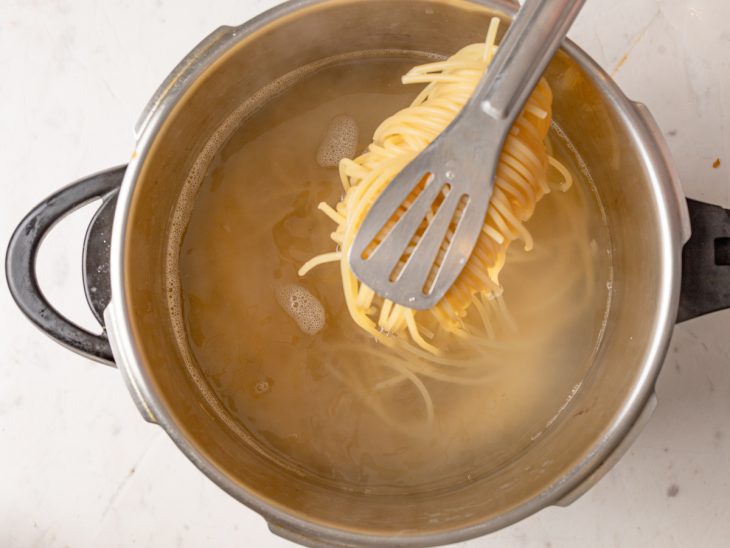 Porção de macarrão cozido em um pegador sobre uma panela com água.