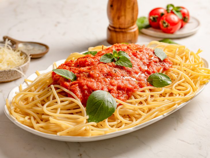 Macarrão ao sugo finalizado com manjericão, pronto para consumo.